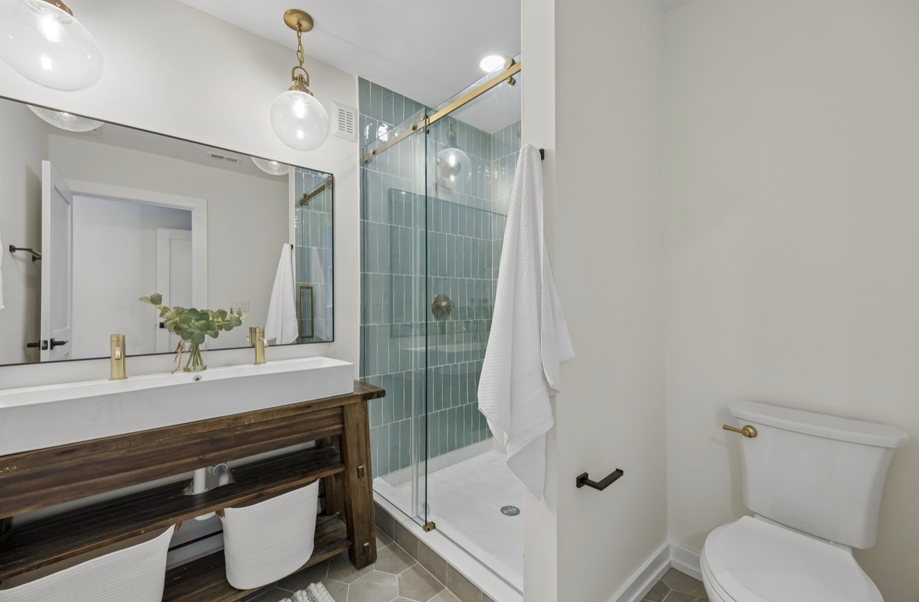 Bathroom with glass shower, sea glass tile, brass faucets, and wood vanity