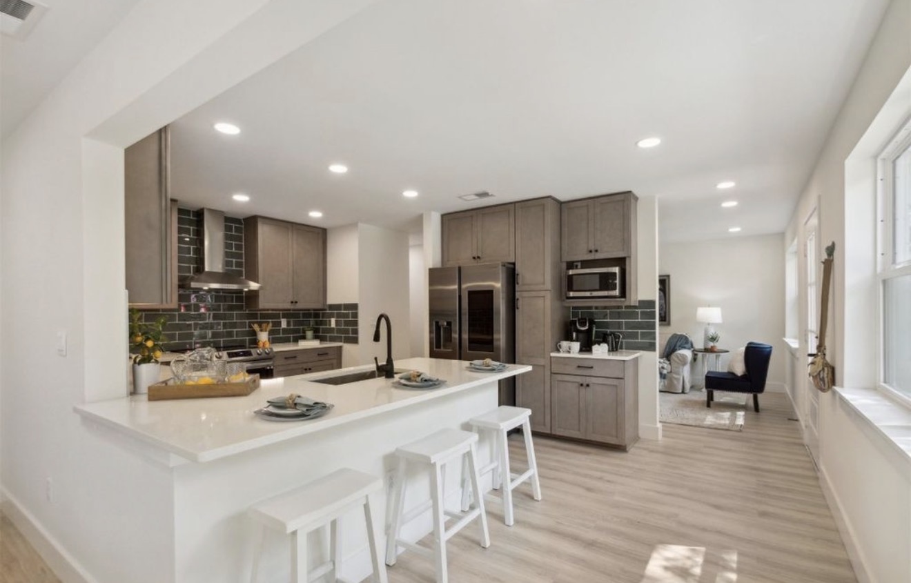 Open kitchen with greige cabinetry, deep green subway tile, and quartz peninsula