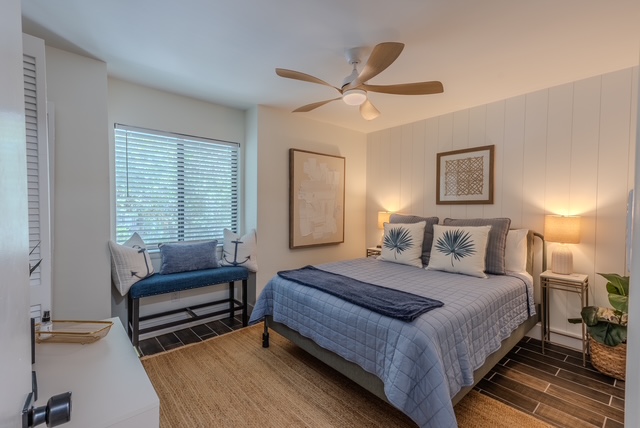 Primary bedroom styled with a blue quilt, coastal pillows, and a window bench