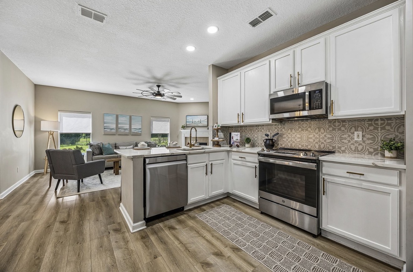 White kitchen with stainless appliances, patterned tile backsplash, and a peninsula open to the living room