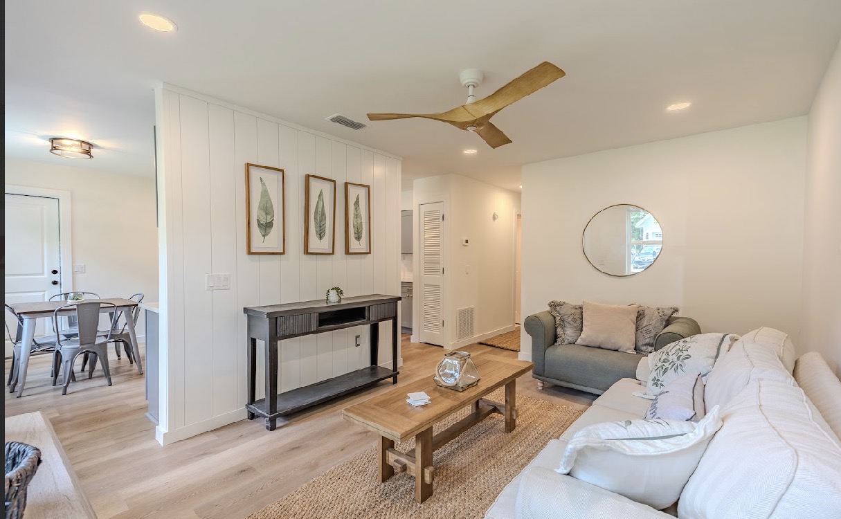 Open living and dining area with cream sofa, sage armchair, shiplap divider wall, and round gold-framed mirror