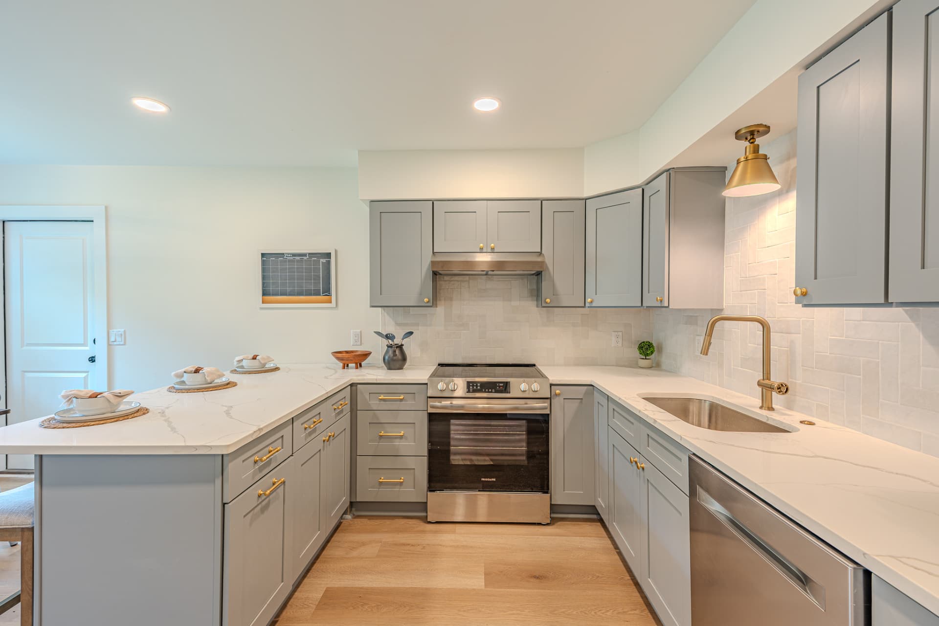 Kitchen with quartz counters, herringbone tile backsplash, brass fixtures, and stainless appliances