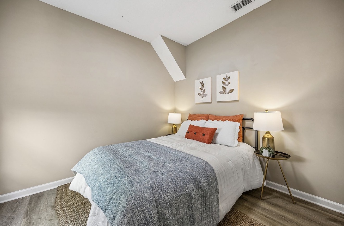 Guest bedroom with grey quilt, terracotta accent pillows, and brass lamps