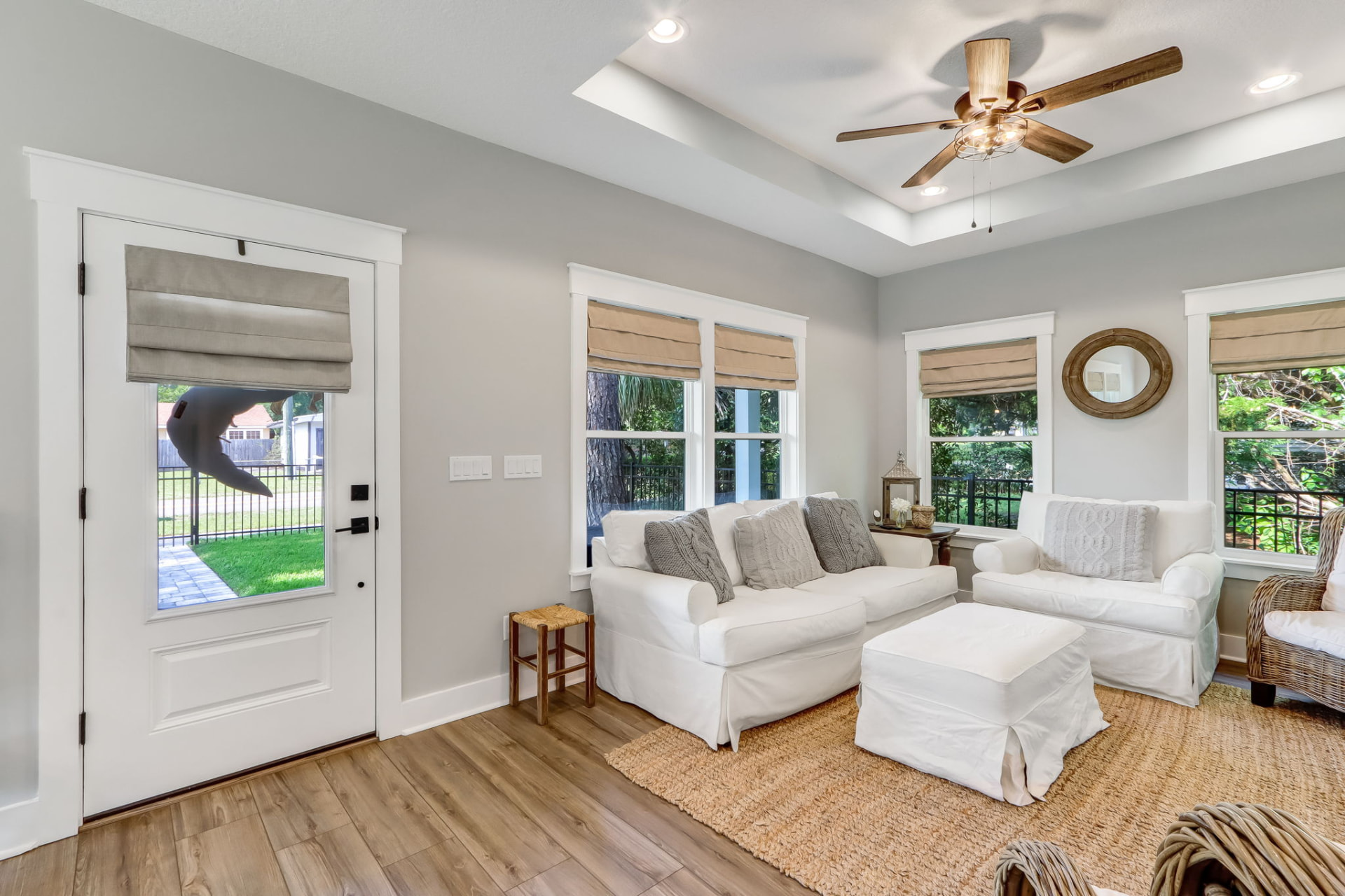 Living room staged with white slipcovered sofa, ottoman, and jute rug beside sunlit windows