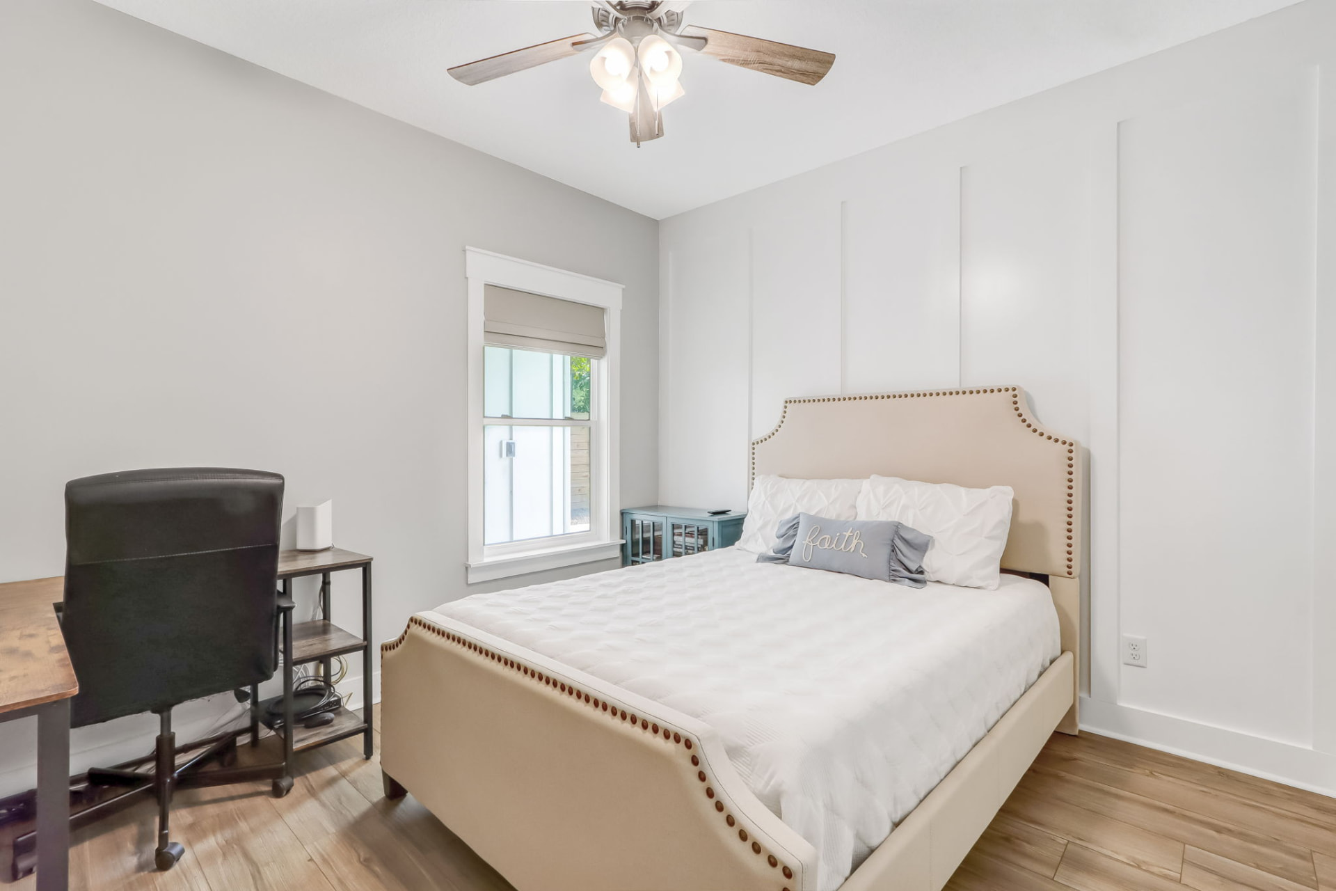 Guest bedroom staged with an upholstered nailhead bed and desk workspace