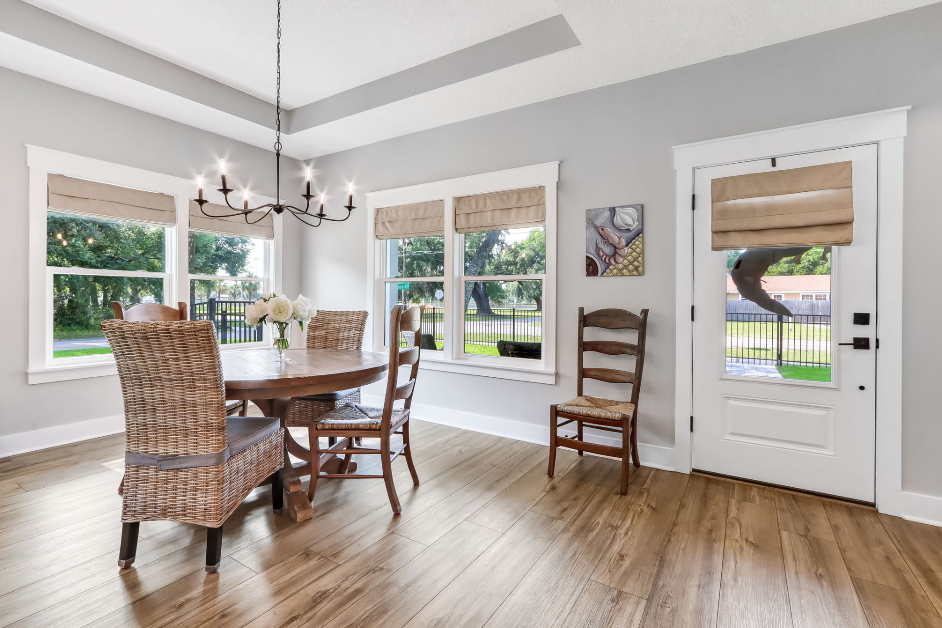 Dining area with round pedestal table, wicker chairs, and iron chandelier