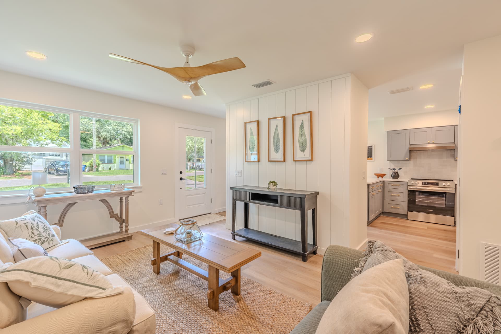Open living area looking toward the entry and kitchen with shiplap accent wall and botanical prints