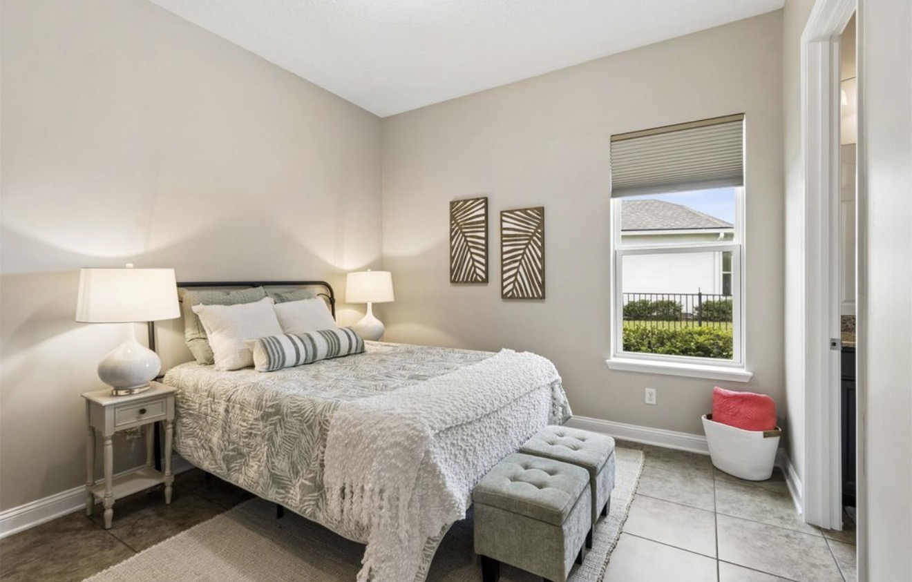Guest bedroom with botanical bedding, ceramic lamps, and tufted ottomans