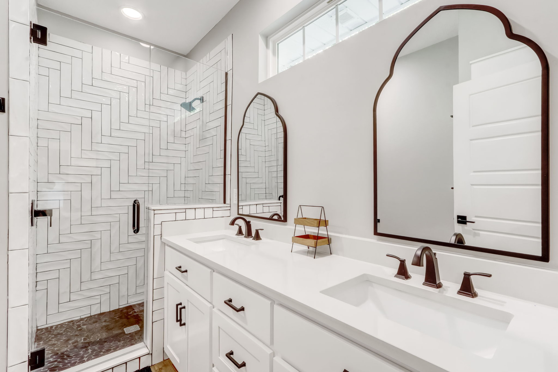 Primary bathroom with double quartz vanity, arched mirrors, and herringbone tile shower