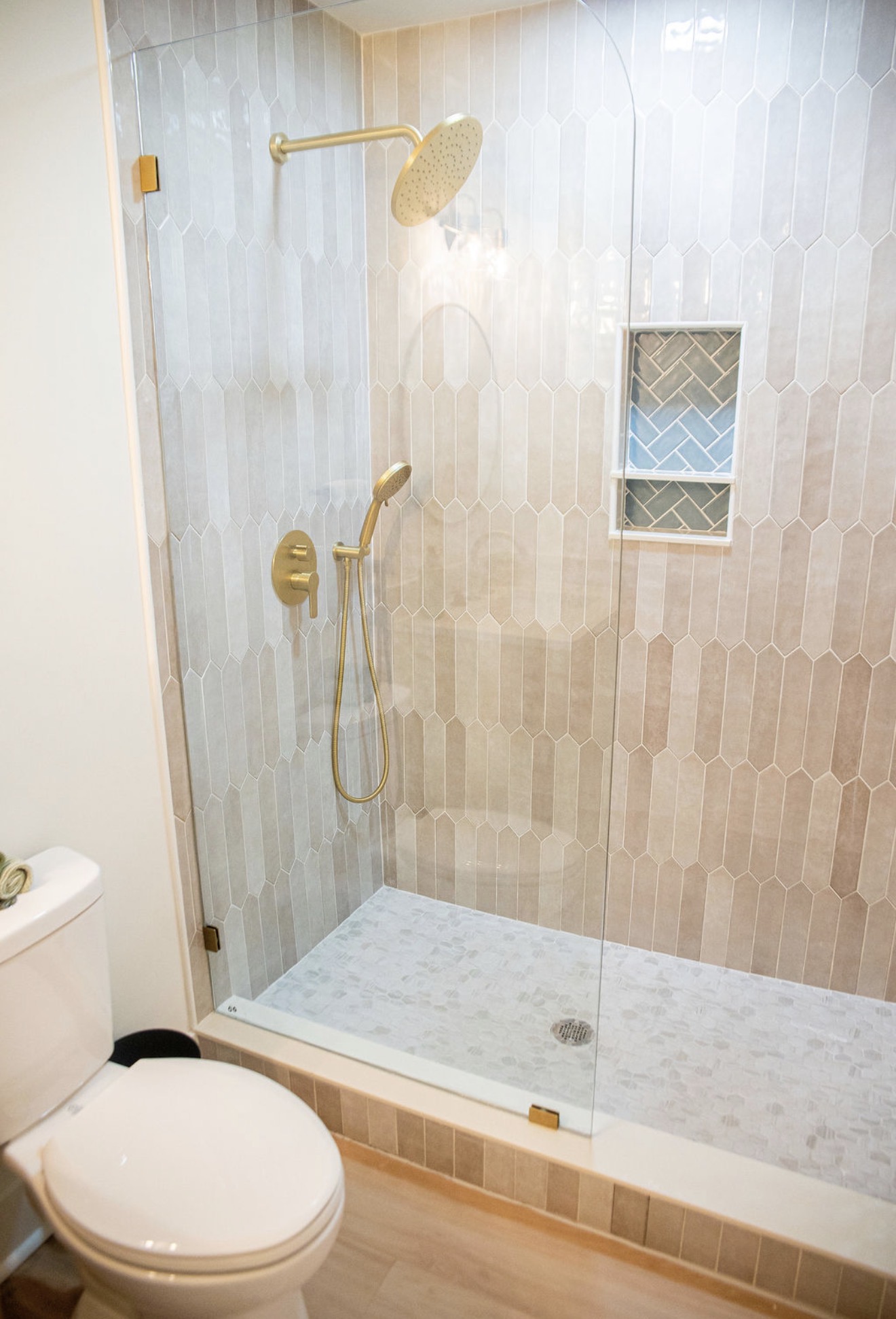 Walk-in shower with blush picket tile, pebble floor, and brushed brass fixtures