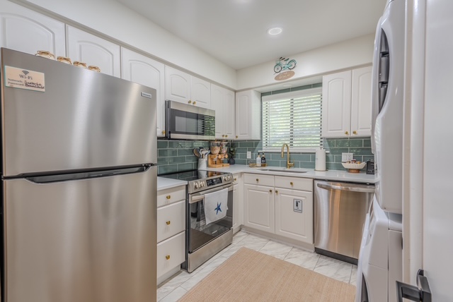 Bright white kitchen with sea-glass tile backsplash, stainless appliances, and brass faucet