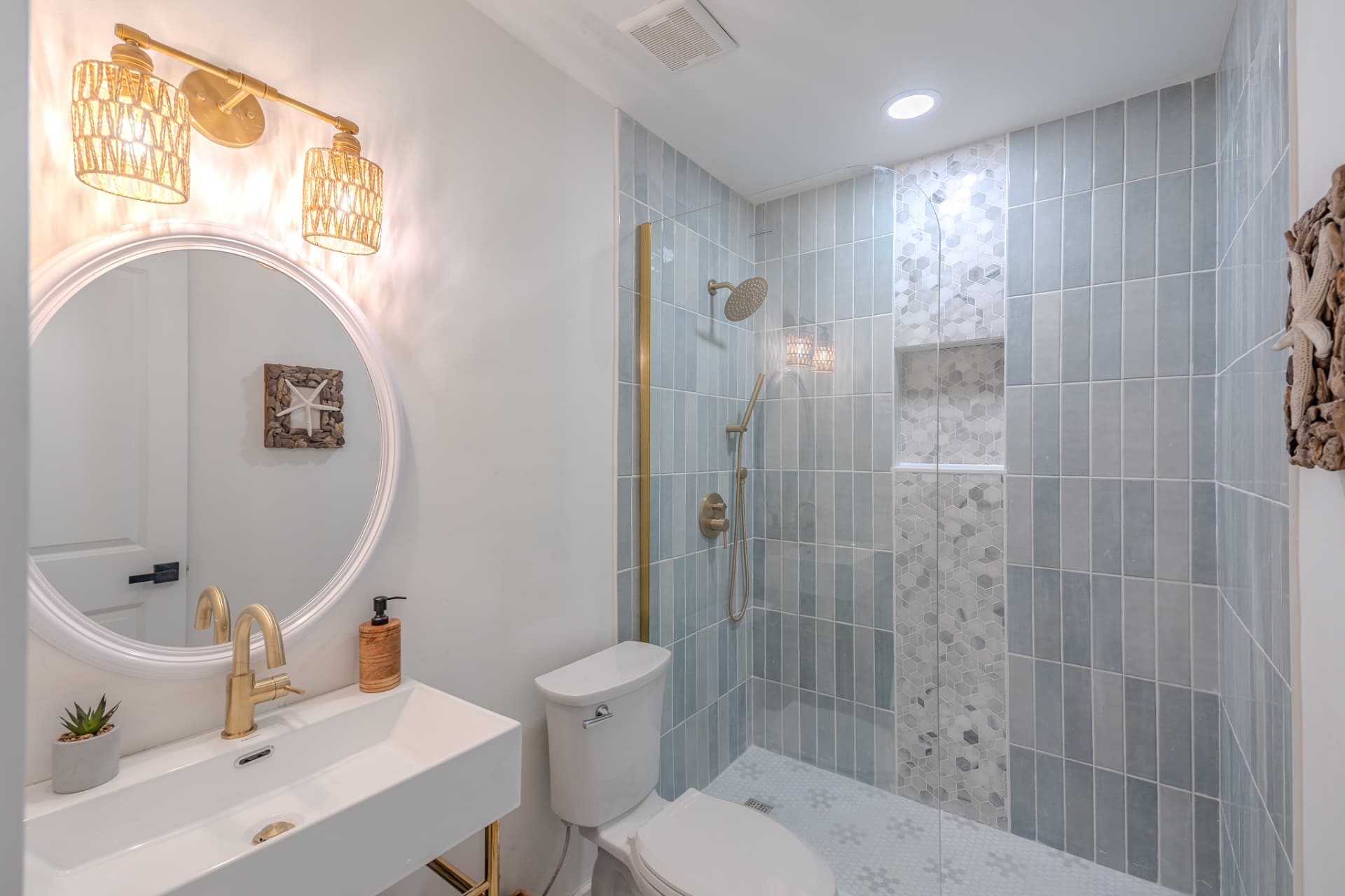 Bathroom with blue vertical tile shower, round mirror, and brass fixtures