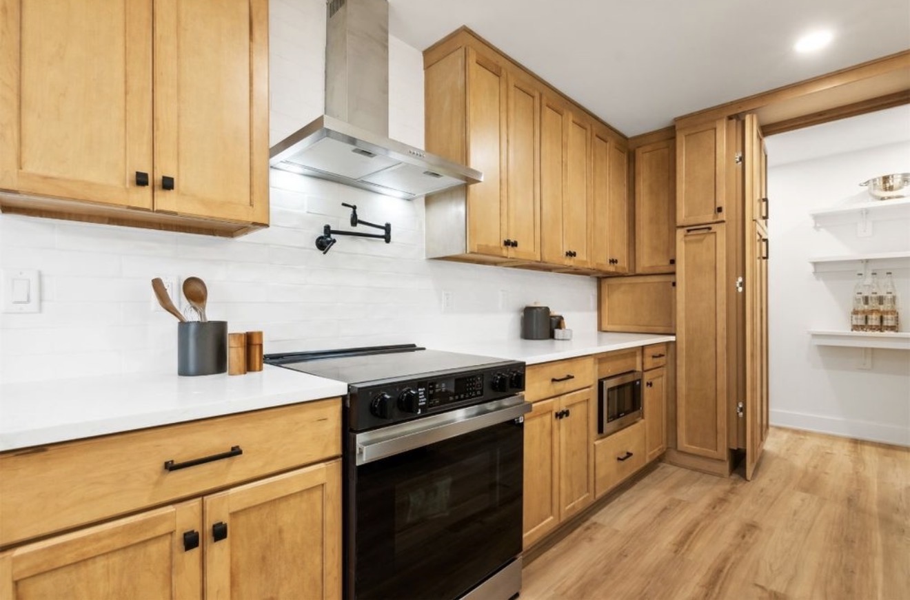 Kitchen with natural maple cabinetry, stainless hood, pot filler, and quartz counters