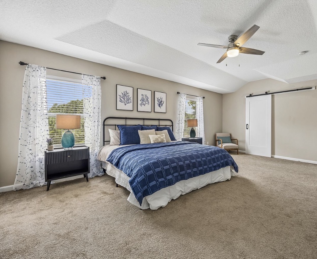 Primary bedroom staged with a blue quilted bed and coastal artwork