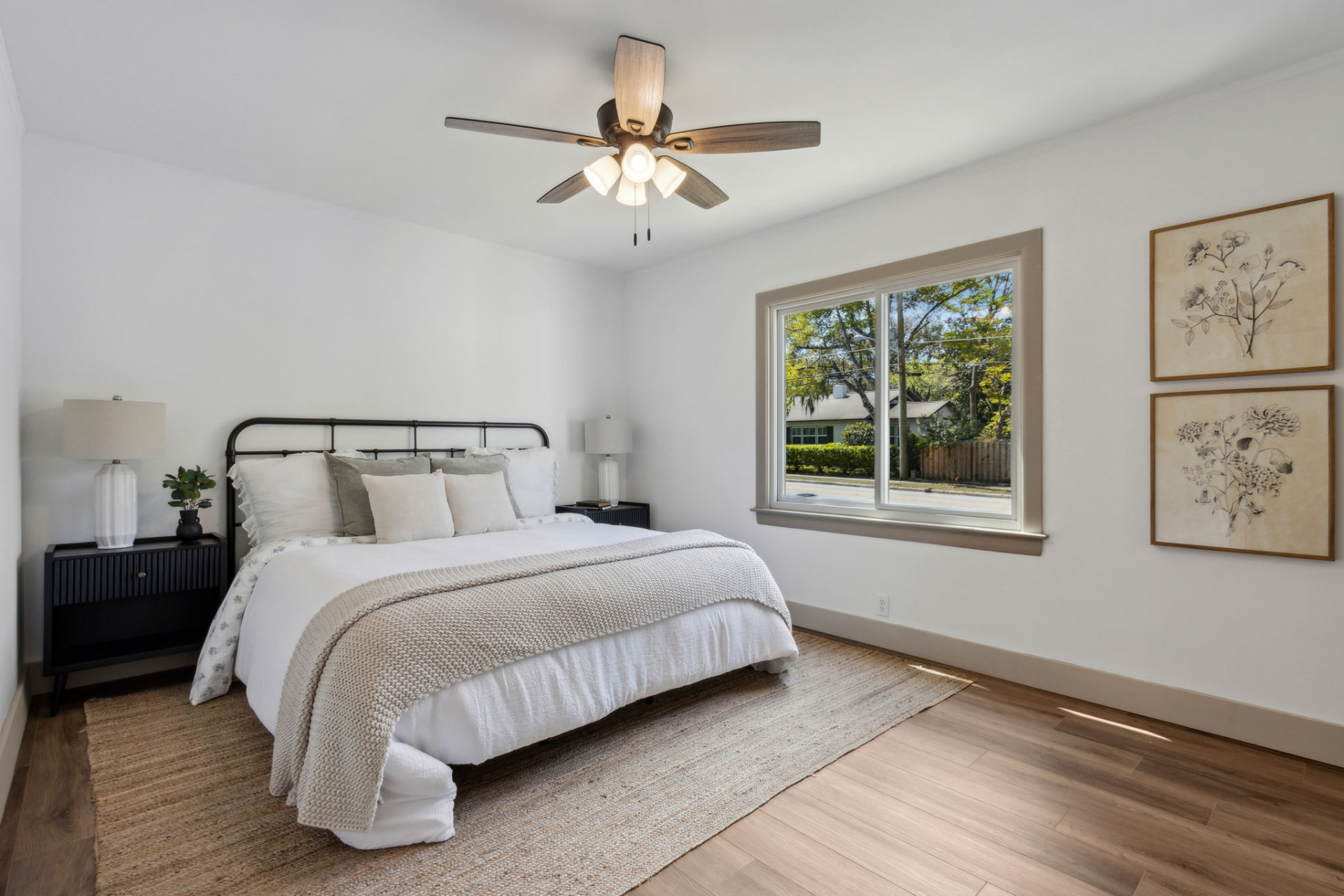 Primary bedroom staged with a black iron bed, layered linens, and botanical art