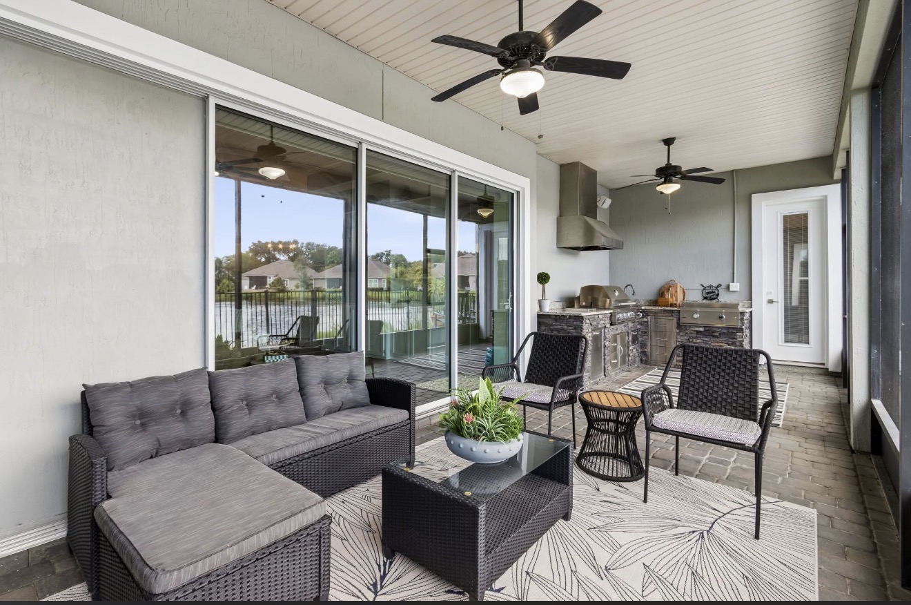 Screened lanai with wicker lounge seating, outdoor kitchen, and lake view