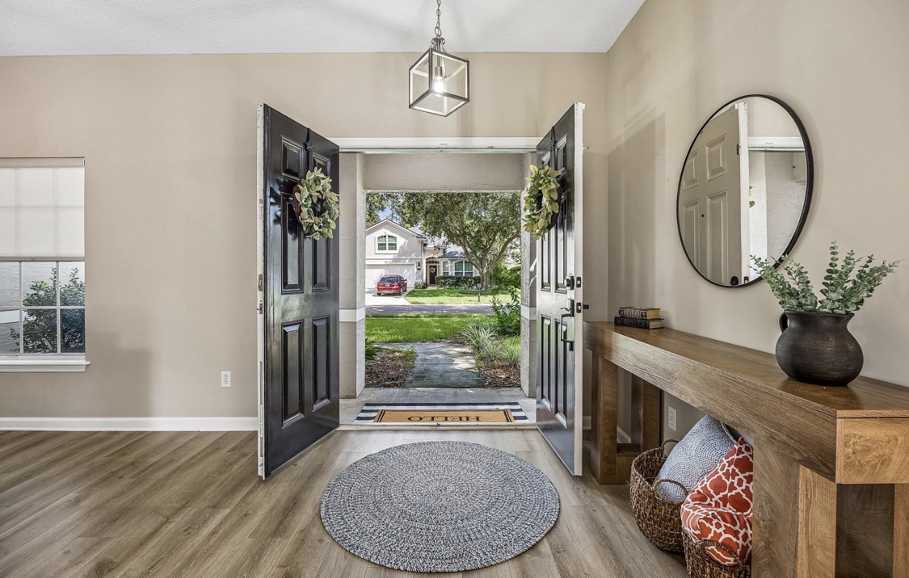 Entry foyer with double black doors, greenery wreaths, round mirror, and a wood console