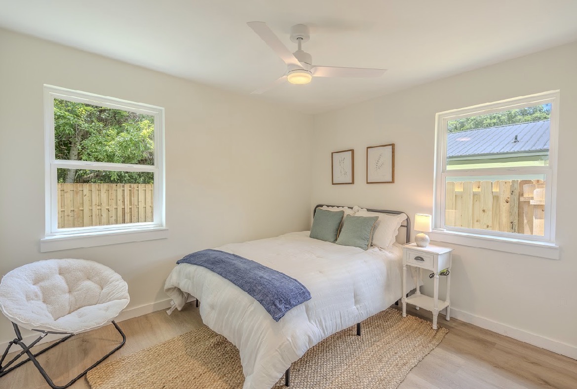 Secondary bedroom staged with white bedding, sage and navy accents, botanical prints, and a jute rug
