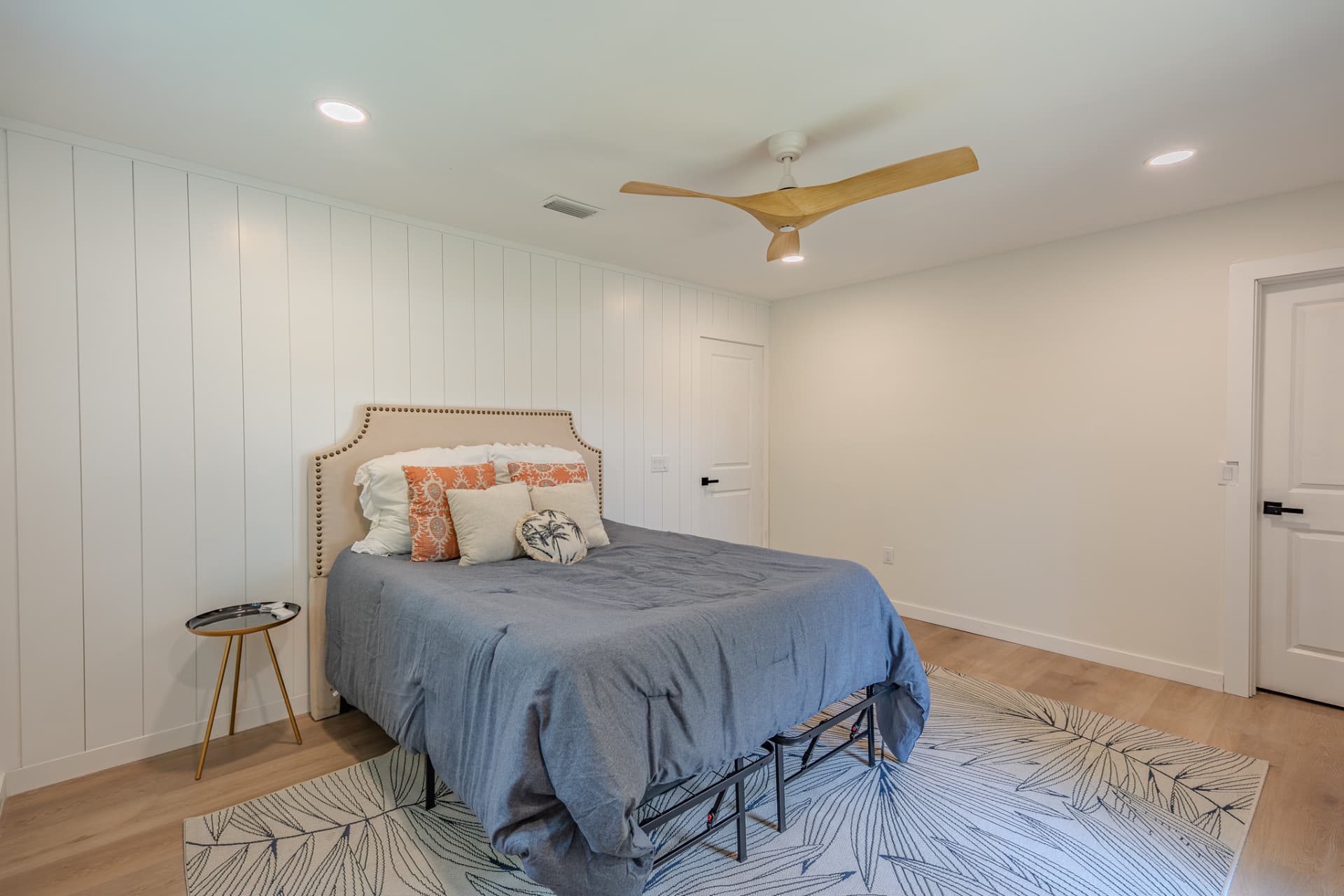 Primary bedroom with upholstered nailhead bed, chambray bedding, and vertical shiplap wall