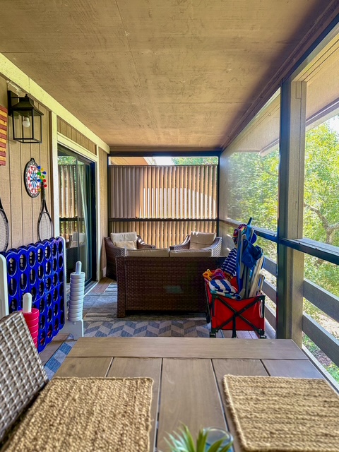 Screened porch lounge with wicker seating, beach chairs, and an outdoor rug