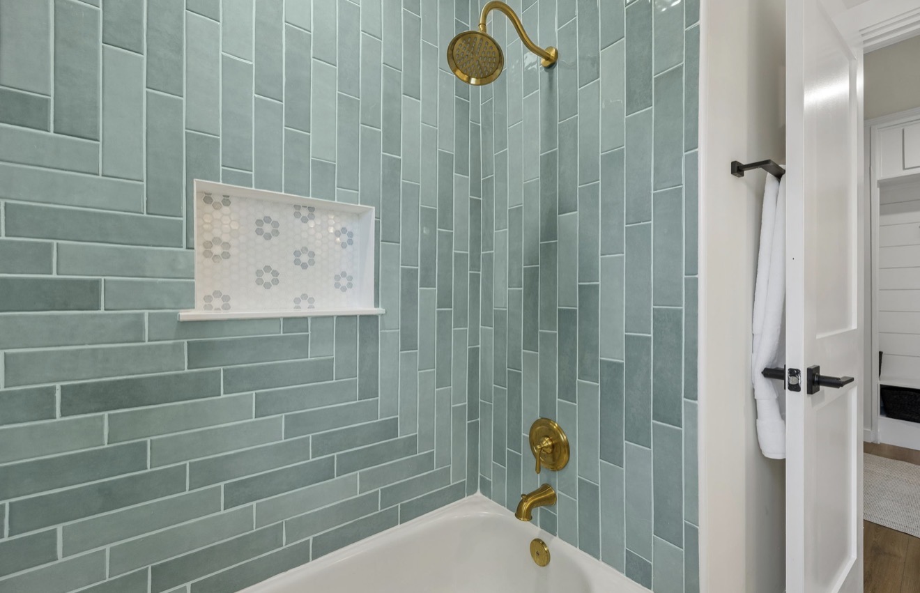 Tub and shower surround in sea glass green tile with brass fixtures
