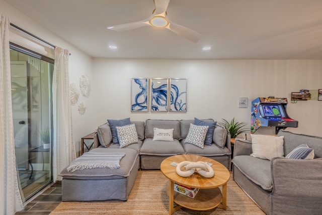 Living room styled with a grey sectional, coastal triptych art, and jute rug in an Amelia Island rental