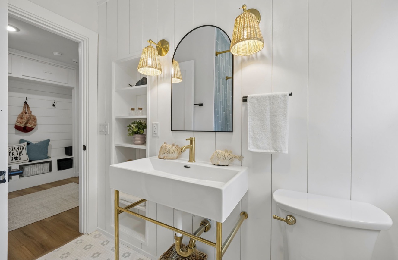 Powder room with shiplap walls, brass console sink, and rattan sconces