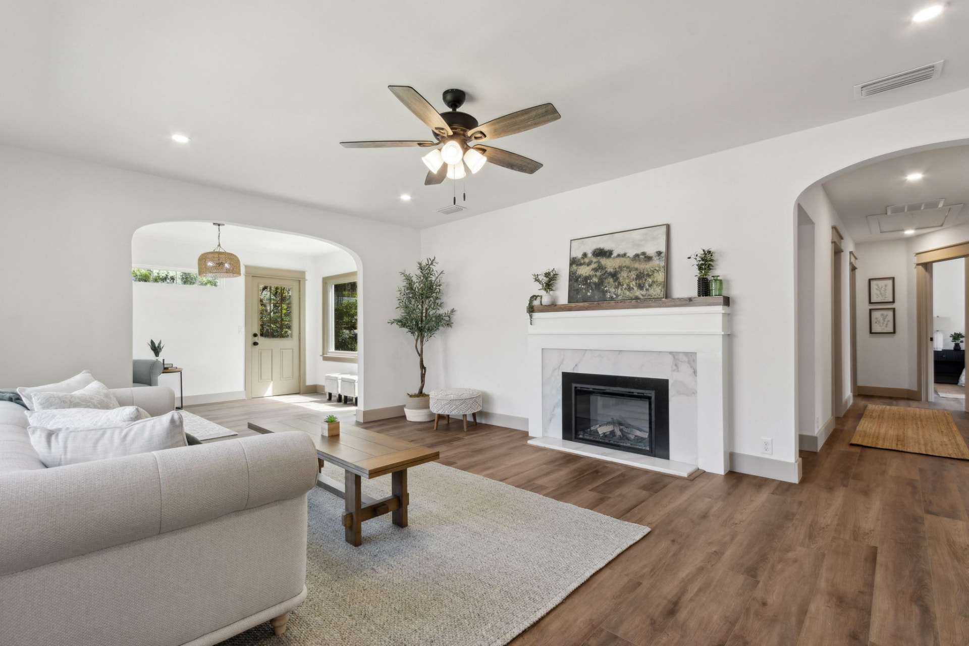 Staged living room with marble fireplace, olive tree, and layered neutral seating