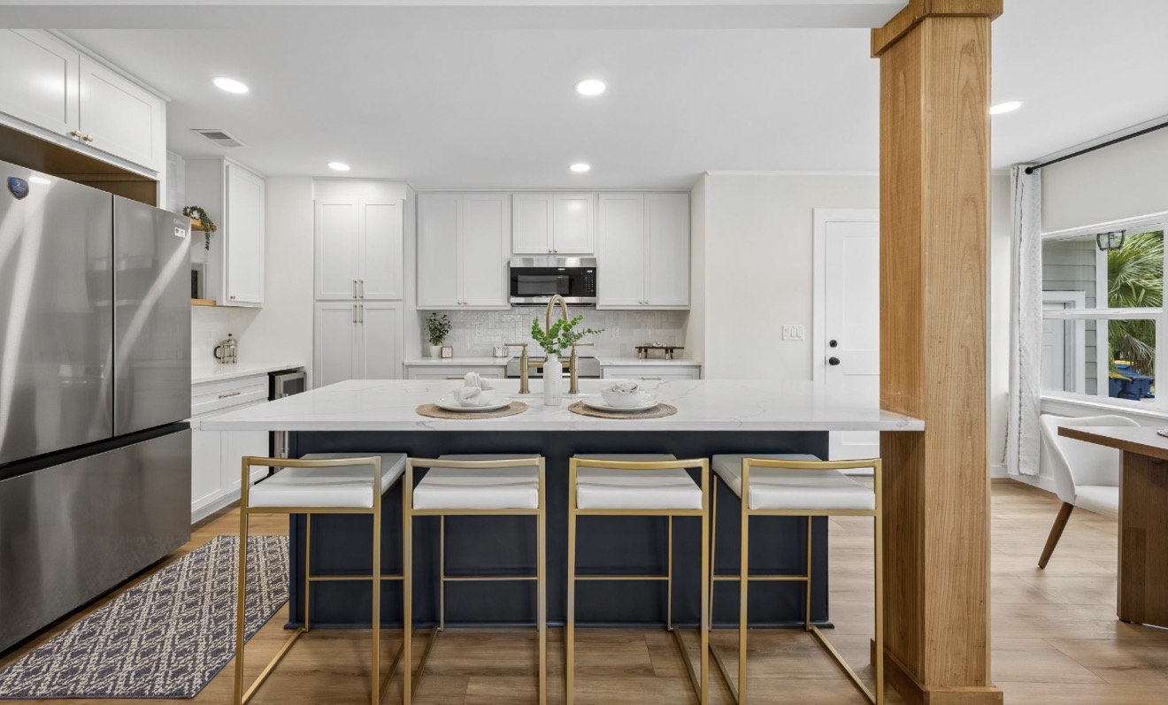 White kitchen with navy quartz island, brass counter stools, and gold fixtures